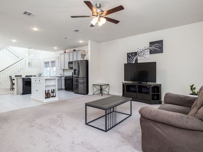 Living room with ceiling fan, stairs, a chandelier, light colored carpet, and light tile patterned floors | Image 4