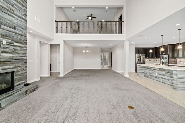 Unfurnished living room with a tiled fireplace, baseboards, ceiling fan with notable chandelier, and a towering ceiling | Image 14
