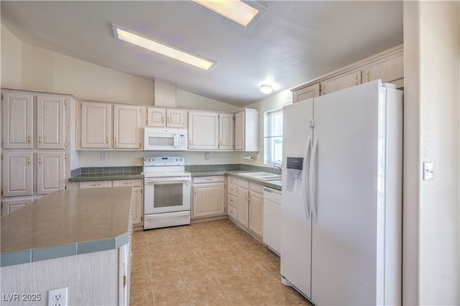 Kitchen with white appliances, lofted ceiling, a sink, and light tile patterned flooring | Image 15
