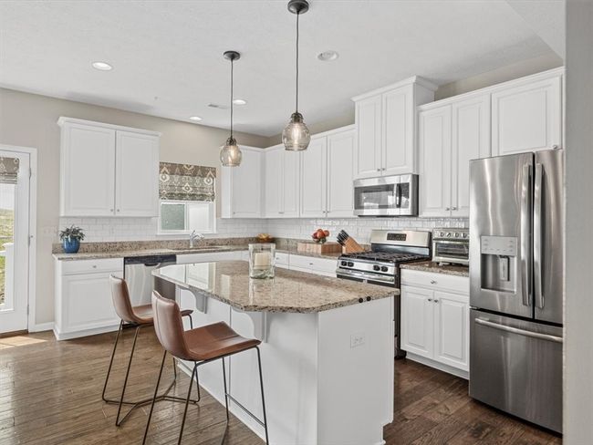 A spacious center island with seating, stylish pendant lighting, and an adjacent dining area create the perfect space for cooking, casual dining, and entertaining with ease. | Image 7