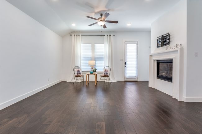 The living room features elegant dark wood-style flooring, a glass-enclosed fireplace, a ceiling fan, and baseboards. | Image 9