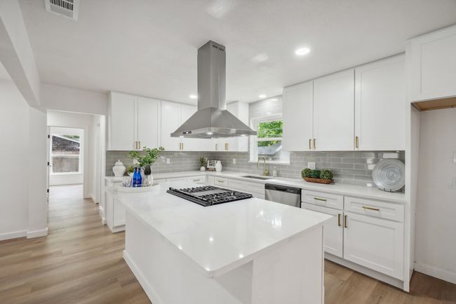 Kitchen featuring island range hood, dishwasher, a sink, black cooktop, and tasteful backsplash | Image 15