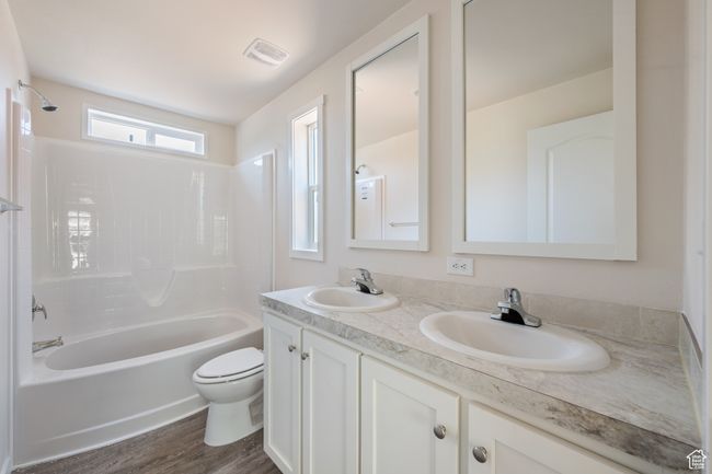Bathroom featuring toilet, double vanity, shower / bathtub combination, and wood finished floors | Image 13