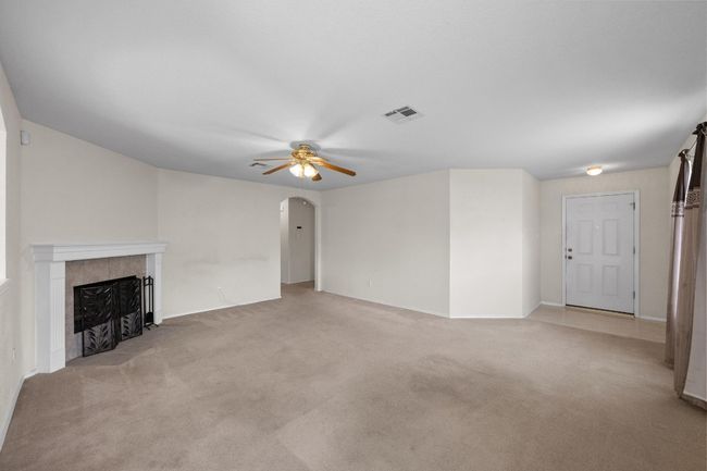 Unfurnished living room featuring a ceiling fan, light carpet, a tile fireplace, arched walkways, and baseboards | Image 5