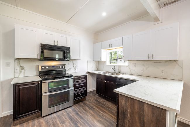 Kitchen with a sink, dark wood finished floors, black appliances, white cabinetry, and backsplash | Image 8