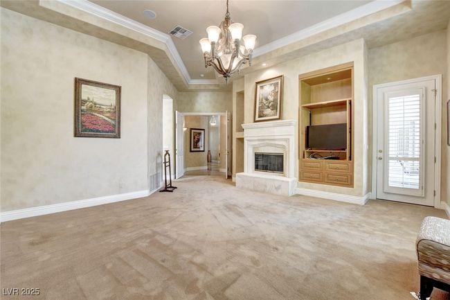Unfurnished living room featuring built in shelves, baseboards, visible vents, a notable chandelier, and crown molding | Image 27