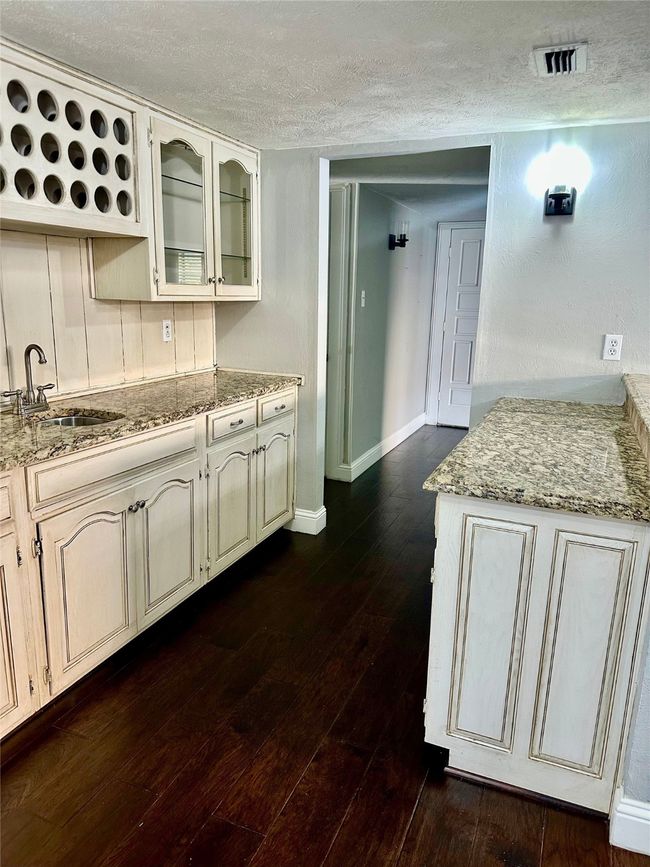 Wet Bar with a textured ceiling, dark wood-type flooring, glass insert cabinets, light stone counters, and cream cabinetry | Image 10