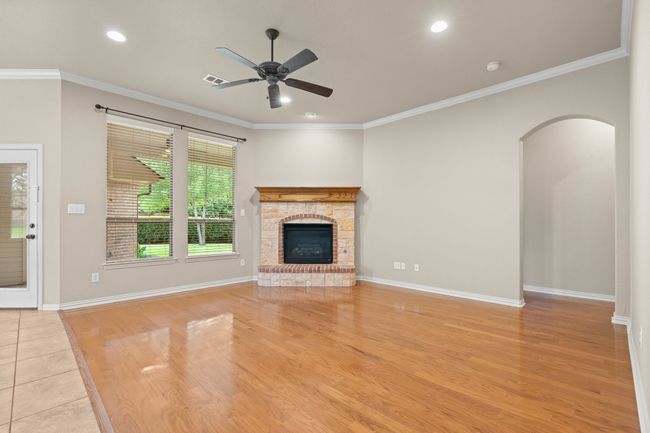 Unfurnished living room featuring a ceiling fan, light wood-style floors, a stone fireplace, recessed lighting, and ornamental molding | Image 10