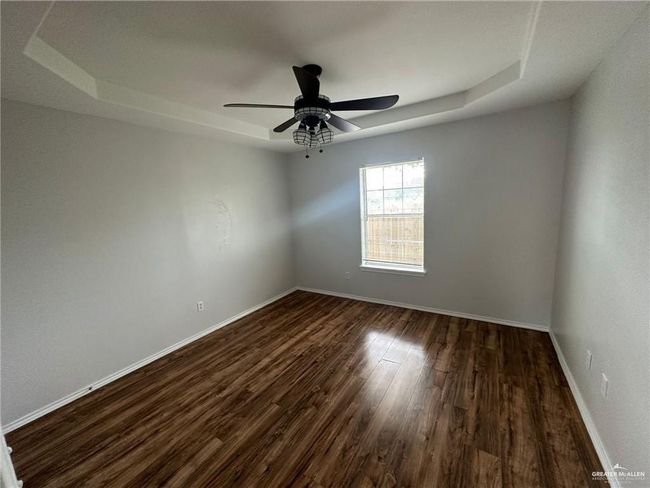 Unfurnished room with ceiling fan, a raised ceiling, baseboards, and dark wood-style flooring | Image 5