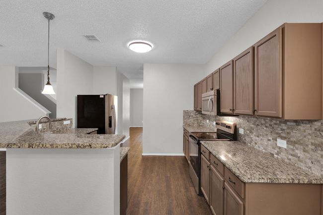 Kitchen with appliances with stainless steel finishes, dark wood-style flooring, decorative backsplash, a textured ceiling, and pendant lighting | Image 11