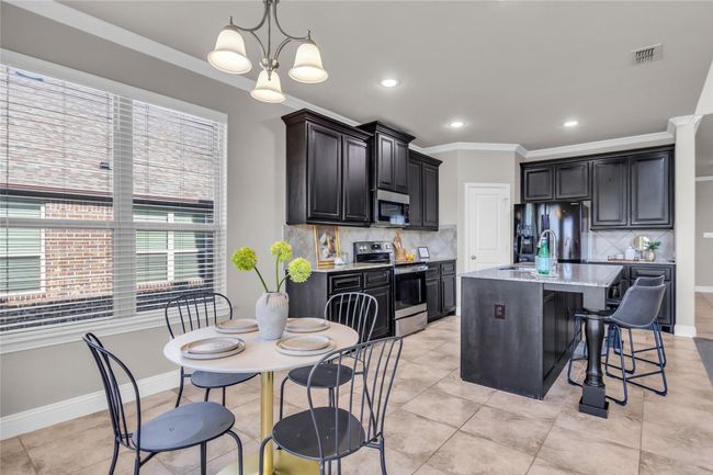 Kitchen with appliances with stainless steel finishes, ornamental molding, backsplash, a kitchen bar, and light stone countertops | Image 6