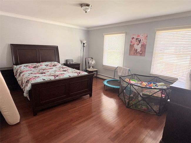 Bedroom featuring wood finished floors, crown molding, and a baseboard heating unit | Image 7