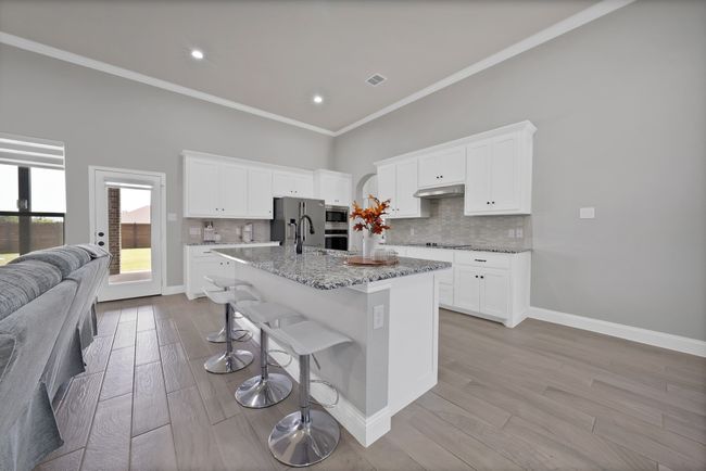 Kitchen featuring under cabinet range hood, a breakfast bar area, tasteful backsplash, stainless steel appliances, and light stone counters | Image 8