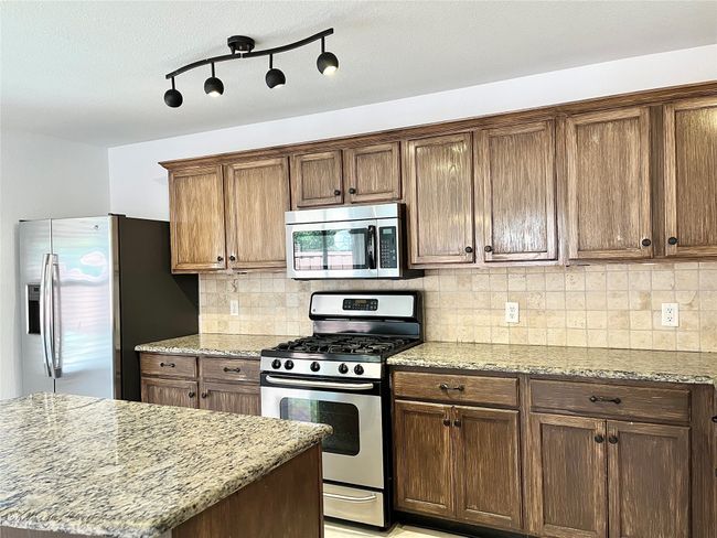 Kitchen with stainless steel appliances, backsplash, and light stone counters | Image 9
