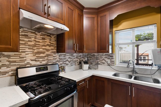 Kitchen with gas stove, range hood, a sink, decorative backsplash, and light countertops | Image 13