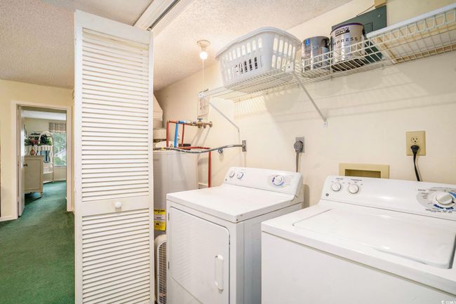 Laundry area featuring washing machine and clothes dryer, dark colored carpet, a textured ceiling, and water heater | Image 17