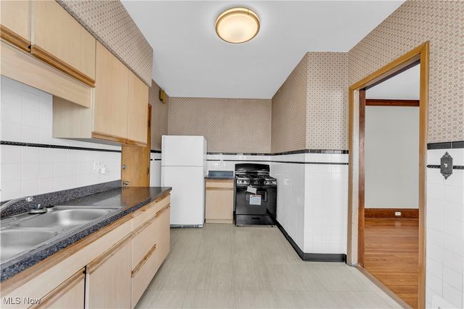 Kitchen featuring freestanding refrigerator, light brown cabinetry, wallpapered walls, black gas range oven, and a sink | Image 13