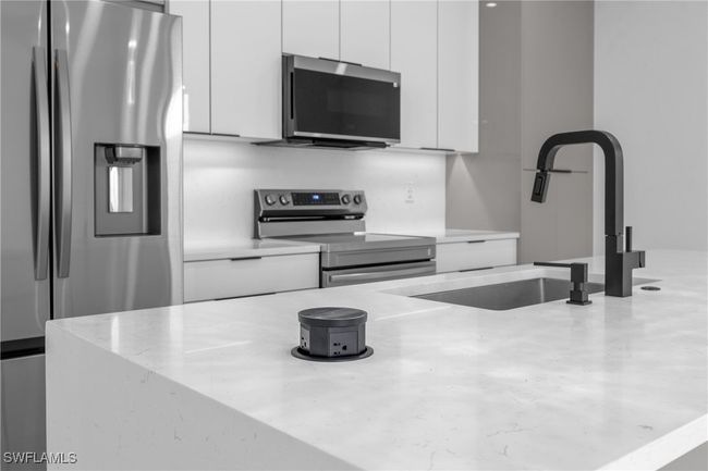 Kitchen with appliances with stainless steel finishes, white cabinets, modern cabinets, light stone countertops, and a sink | Image 10