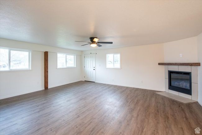 Unfurnished living room with baseboards, ceiling fan, a tiled fireplace, and wood finished floors | Image 15