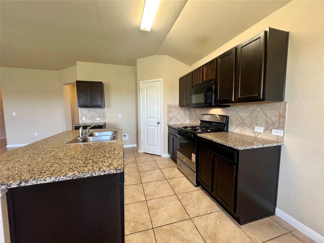 Kitchen featuring gas range, a sink, black microwave, tasteful backsplash, and light tile patterned flooring | Image 24