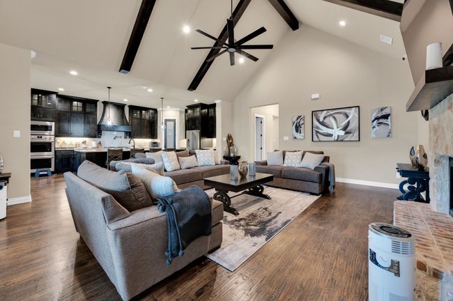 Living room featuring high vaulted ceiling, beamed ceiling, a ceiling fan, dark wood finished floors, and a fireplace with raised hearth | Image 13
