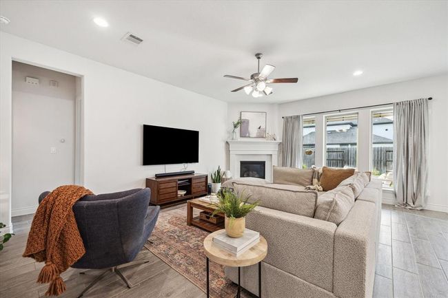 The spacious living room features a cozy corner fireplace that serves as a striking focal point, while large windows invite abundant natural light and picturesque outdoor views, enhancing the room’s warm and inviting ambiance. | Image 9