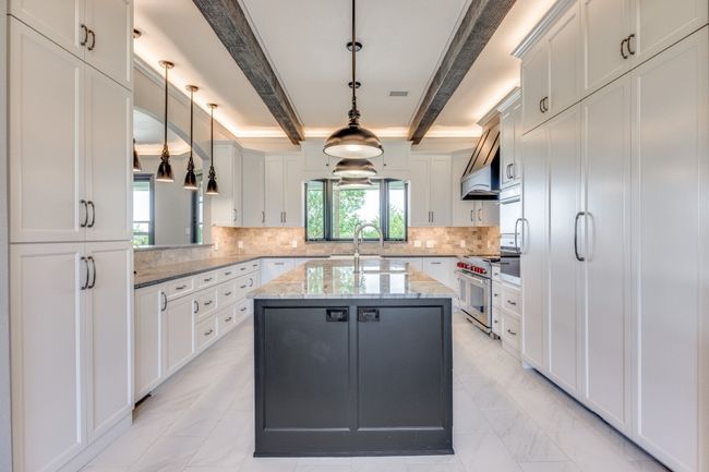 Kitchen with beam ceiling, a center island with sink, range with two ovens, hanging light fixtures, and light marble finish floors | Image 6