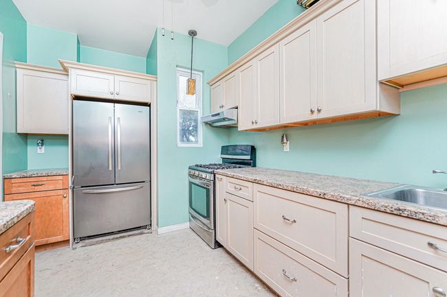 Kitchen featuring stainless steel appliances, under cabinet range hood, hanging light fixtures, and light floors | Image 6