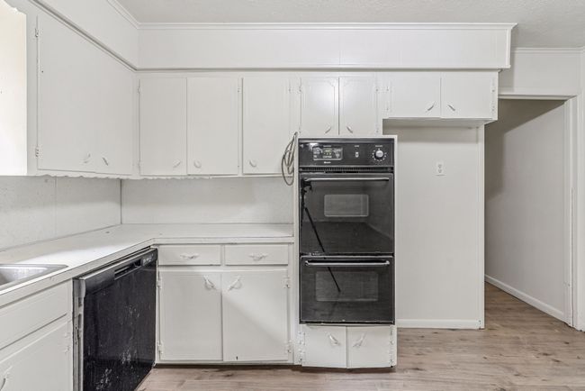 Kitchen featuring black appliances, light wood-type flooring, light countertops, white cabinetry, and ornamental molding | Image 16