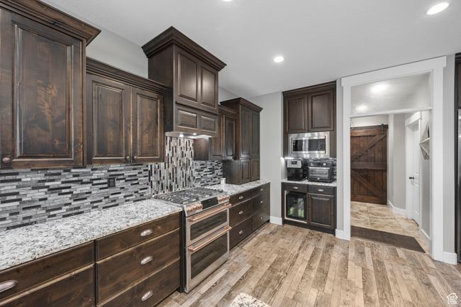 Kitchen with appliances with stainless steel finishes, dark brown cabinets, vented hood, baseboards, backsplash, and light wood-style flooring | Image 10