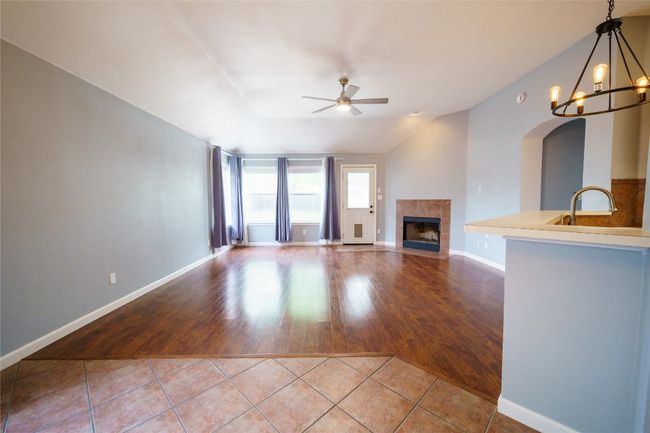 Living room with ceiling fan, a tile fireplace, tile patterned floors, a chandelier, and arched walkways | Image 8