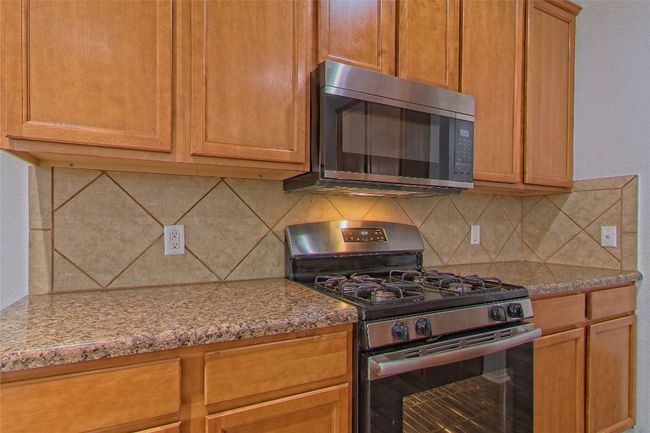 Kitchen featuring stainless steel appliances, decorative backsplash, and light stone countertops | Image 14