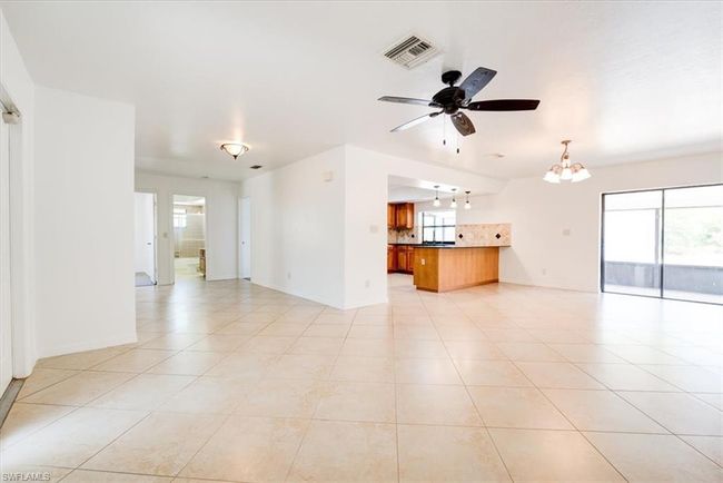 Unfurnished living room featuring baseboards, visible vents, light tile patterned floors, and ceiling fan with notable chandelier | Image 8