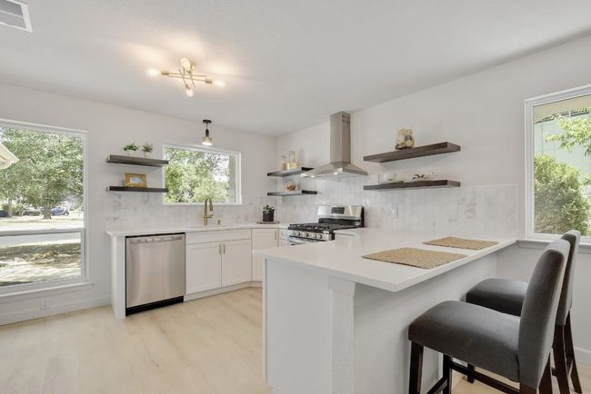 Newly remodeled kitchen features American Woodmark lower cabinets with corner Lazy Susan cabinets, floating shelves, white quartz countertops, a Carrara marble backsplash, stainless-steel dishwasher and gas range, modern fixtures, and a vented, stainless steel range hood. | Image 8