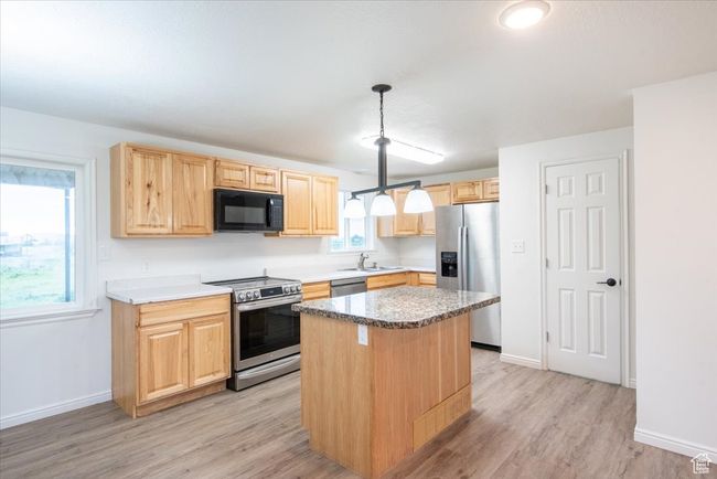 Kitchen with a kitchen island, light brown cabinets, light wood-style floors, a sink, and stainless steel appliances | Image 11