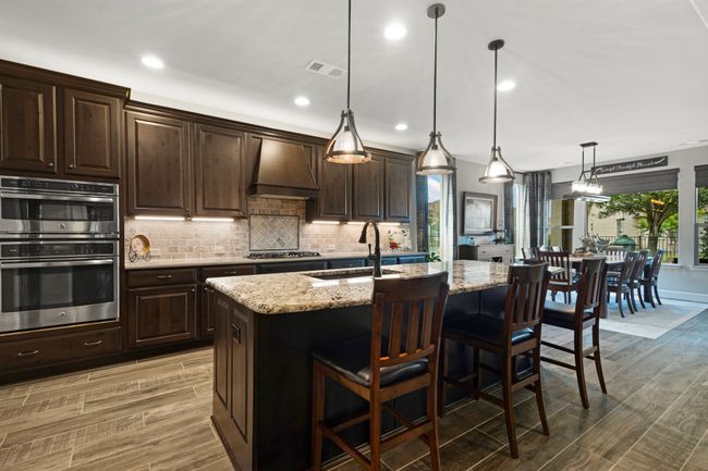 Kitchen featuring stainless steel appliances, a sink, custom exhaust hood, light stone countertops, and tasteful backsplash | Image 13