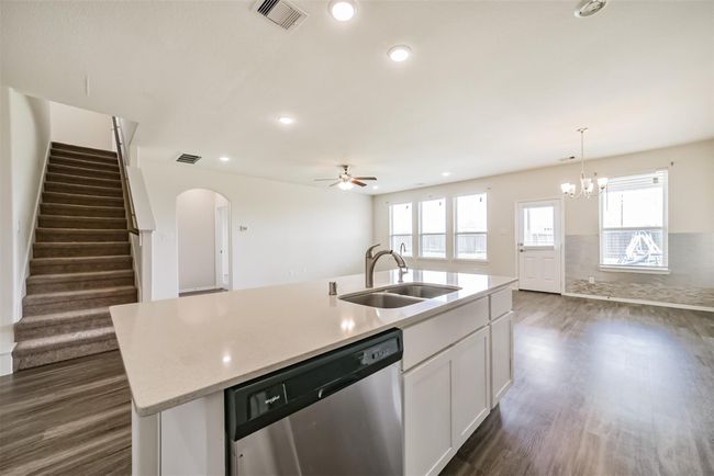 This photo showcases a spacious, open-concept living area with a modern kitchen featuring an island, stainless steel appliances, and ample natural light. The room includes a dining area, large windows, and access to an outdoor space. A staircase leads to the upper floor. | Image 15