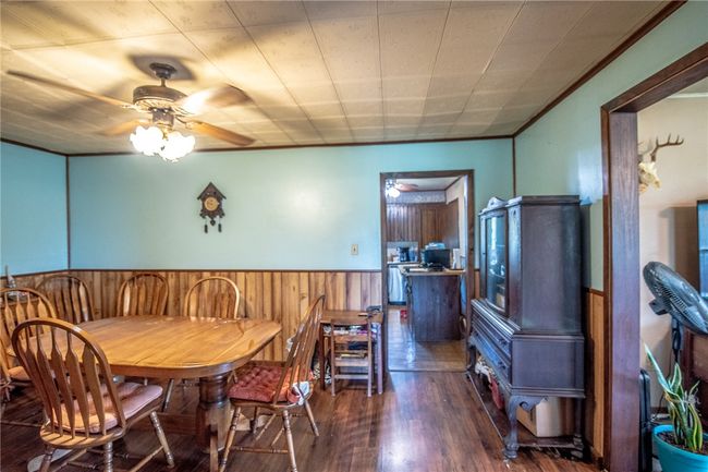 Dining area featuring a ceiling fan, a wainscoted wall, wood finished floors, wood walls, and a wood stove | Image 17