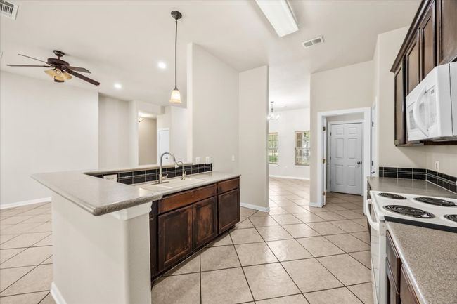 Kitchen with white appliances, light tile patterned floors, dark brown cabinets, ceiling fan, and a sink | Image 12