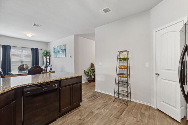 Kitchen featuring black appliances, light wood-vinyl-type flooring, light stone countertops, dark brown cabinetry, and baseboards | Image 25