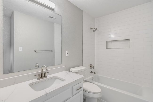 Bathroom with bathing tub / shower combination, vanity, visible vents, toilet, and a textured wall | Image 14