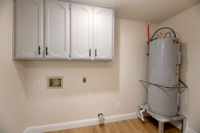 Washroom featuring hookup for an electric dryer, gas water heater, cabinet space, baseboards, and hookup for a washing machine | Image 23