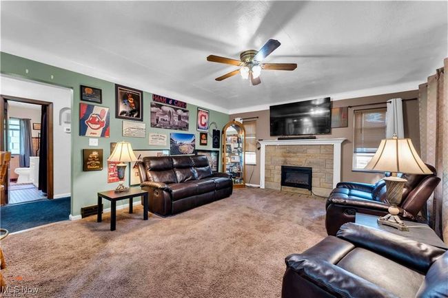 Carpeted living area featuring a ceiling fan, a fireplace, and baseboards | Image 8
