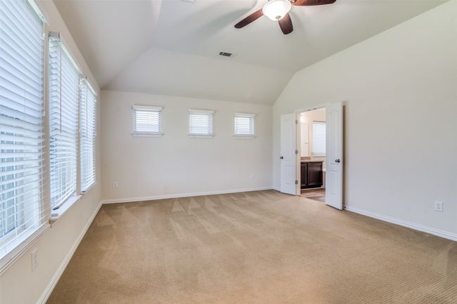 Another view of the primary bedroom featuring light carpet, lofted ceiling, ceiling fan, and ensuite bath | Image 14