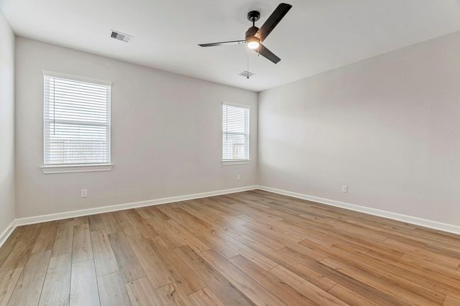 Step into the primary bedroom, where vinyl plank flooring sets the stage for relaxation. Natural light pours in through the windows, creating a warm and relaxing retreat. Tall doors reveals the en-suite bathroom, offering convenience and luxury for the perfect escape. | Image 8