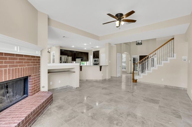 Unfurnished living room featuring arched walkways, baseboards, a brick fireplace, stairs, and ceiling fan | Image 10