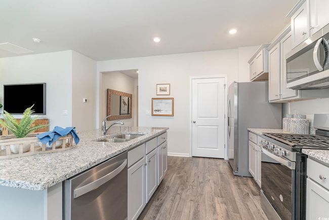 Kitchen with sink, light hardwood / wood-style floors, stainless steel appliances, light stone countertops, and a center island with sink | Image 6