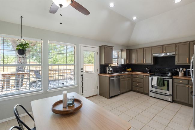Kitchen with appliances with stainless steel finishes, gray cabinets, light tile patterned floors, under cabinet range hood, and lofted ceiling | Image 9