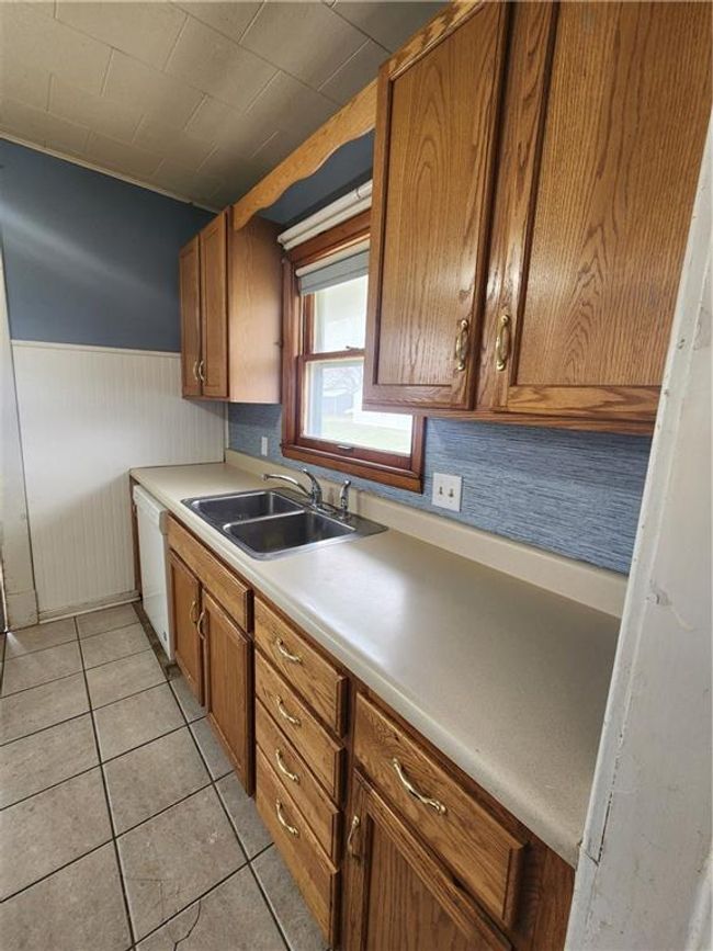 Kitchen featuring wainscoting, dishwasher, a sink, brown cabinetry, and light tile patterned floors | Image 23