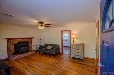 Living room with a wood stove, hardwood / wood-style flooring, and ceiling fan | Image 3